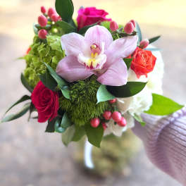 Handheld bouquet with pink orchid, red and orange roses, green blooms, and pink berries