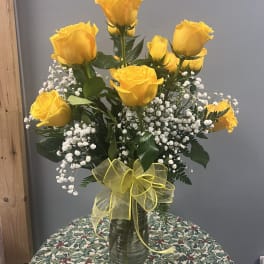 Yellow roses in a glass vase with baby's breath and a yellow ribbon
