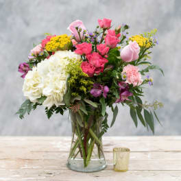 Mixed bouquet of pink, white, and yellow flowers in a glass vase
