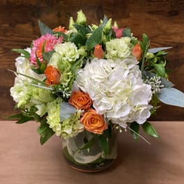 Mixed bouquet of white, pink, orange, and green flowers in a glass vase