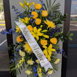 Yellow and blue floral standing spray with a "Beloved Mother" ribbon