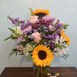 Mixed bouquet in a glass vase with sunflowers, roses, and purple blooms
