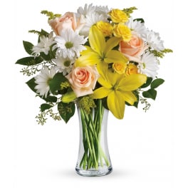 Mixed bouquet of yellow lilies, white daisies, and peach roses in a clear glass vase