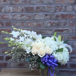 White floral arrangement in a glass vase with a purple ribbon
