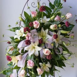 Tall floral spray with white lilies, pink roses, and lavender ribbon on a metal stand