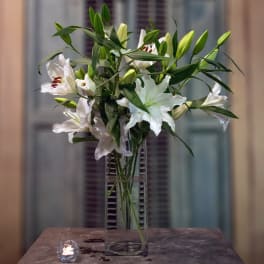 White lilies arranged in a tall clear glass vase