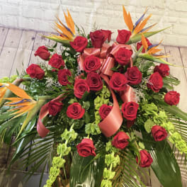 Large bouquet of red roses with orange bird-of-paradise blooms and pink ribbon