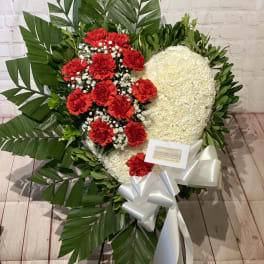 Heart-shaped floral wreath with red and white flowers and a white ribbon