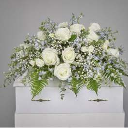 White roses and pale blue flowers arranged on a white casket