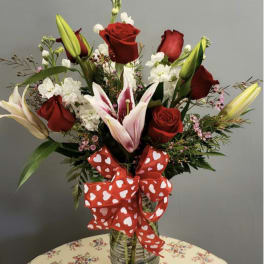 Red roses and lilies in a glass vase with a heart-patterned ribbon