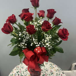 Red roses in a glass vase with baby's breath and a red ribbon