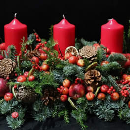 Holiday centerpiece with red candles, pinecones, berries, and evergreen branches