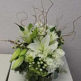 White lily arrangement in a dark round container with curly branches