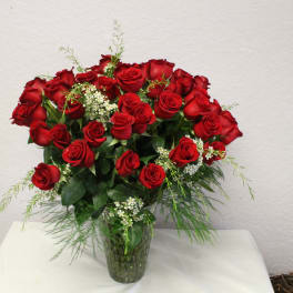 Red roses arranged in a clear glass vase with small white filler flowers
