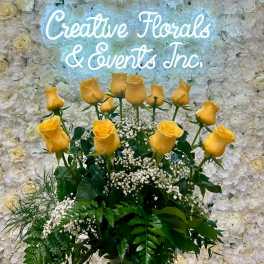 Yellow roses arranged before a white floral wall with a glowing sign