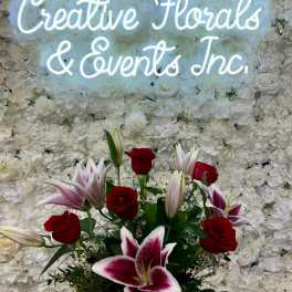 Red roses and pink lilies in front of a white floral wall with neon text
