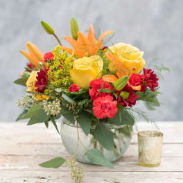 Colorful bouquet of yellow roses, orange lilies, and red daisies in a glass vase