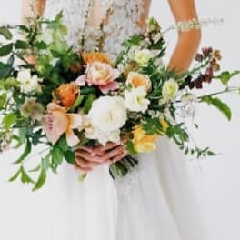 Bride holding a loose bouquet of peach, white, and yellow flowers