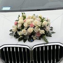 Cream and pink floral arrangement mounted on the hood of a white BMW.