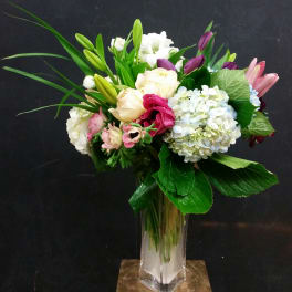Mixed bouquet of white, pink, and purple flowers in a clear glass vase