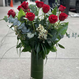 Red roses arranged in a tall glass vase with mixed greenery