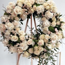 Large cream floral wreath on a wooden stand with trailing greenery