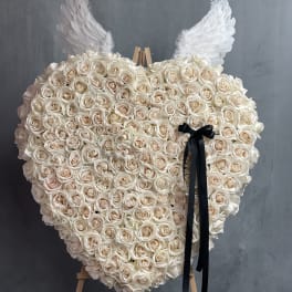 Heart-shaped rose arrangement with white wings and a black ribbon on an easel