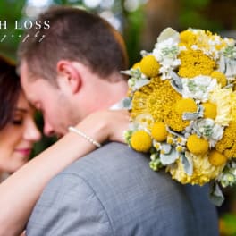 Bride and groom embracing beside a yellow and white bouquet