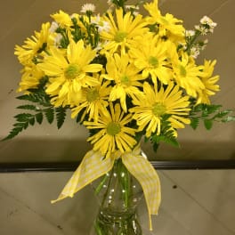 Yellow daisy bouquet in a clear glass vase with a checked ribbon