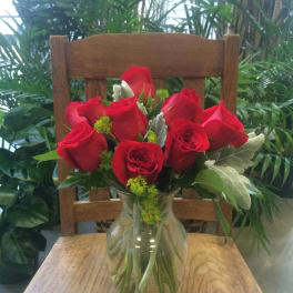 Red roses arranged in a clear glass vase on a wooden chair