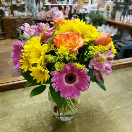 Mixed bouquet of pink, yellow, and orange flowers in a glass vase