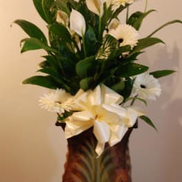 White flowers arranged in a tall decorative vase with a large ribbon bow