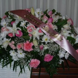 Pink and white funeral spray with a satin ribbon on a casket