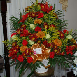 Large red and orange floral arrangement with a gold bow in a white vase