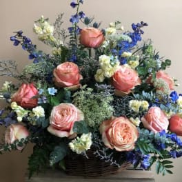 Basket arrangement of peach roses with blue and white flowers