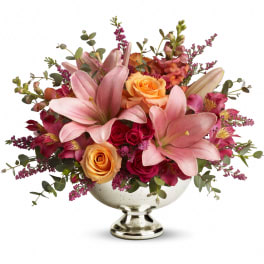 Low centerpiece of pink lilies and orange and dark pink roses in a silver pedestal bowl