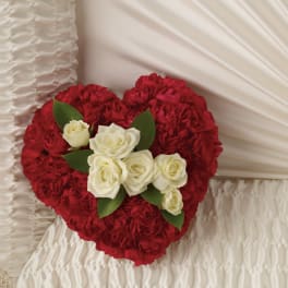 Heart-shaped red carnation arrangement with white roses, displayed against white ruched fabric