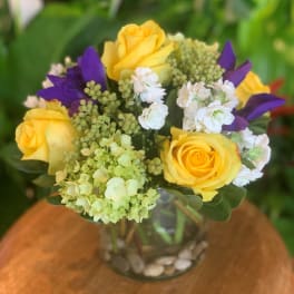 Yellow roses and purple flowers in a glass vase