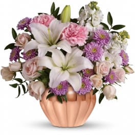 Low arrangement of white lilies, pink carnations, roses and purple mums in a copper pumpkin-shaped vase