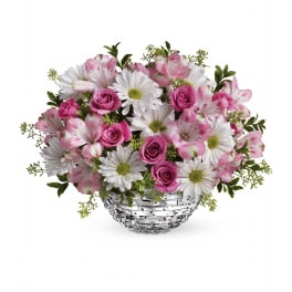 Low round arrangement of pink roses, white daisies, and pink-tipped blooms in a silver woven bowl.
