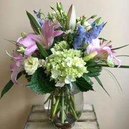 Pink lilies and blue flowers in a clear glass vase