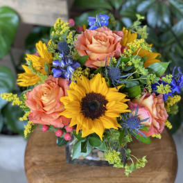Bouquet of sunflowers, peach roses, and blue flowers in a glass vase