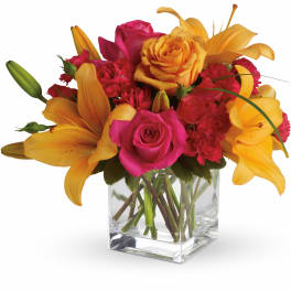 Bright orange lilies and hot pink roses arranged in a clear glass cube vase