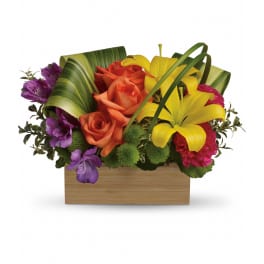 Low rectangular arrangement with yellow lilies, orange roses, and mixed bright blooms in a wooden box