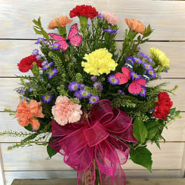 Colorful bouquet of carnations and purple daisies in a glass vase with a pink bow