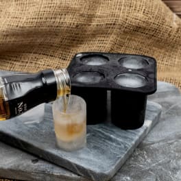 Bottle pouring liquor into a frosted shot glass beside an ice mold
