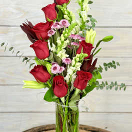 Tall bouquet of red roses, white snapdragons, and pink daisies in a glass vase