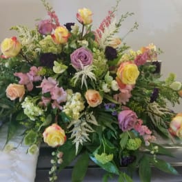 Large mixed floral spray with roses and pastel blooms on a casket