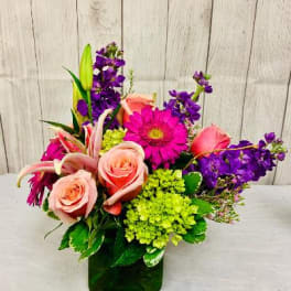 Mixed bouquet of pink roses, purple blooms, and green hydrangea in a glass vase