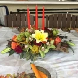Low floral centerpiece with a yellow lily and red candles on a table